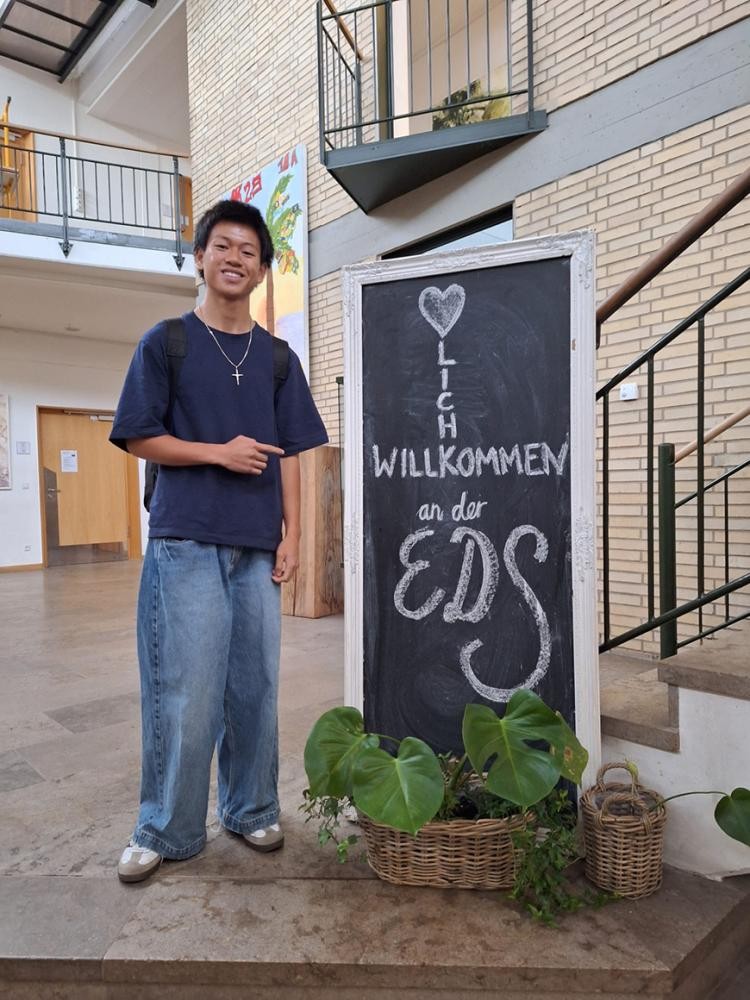 privat Ein junger Mann steht strahlend neben einem Willkommensschild