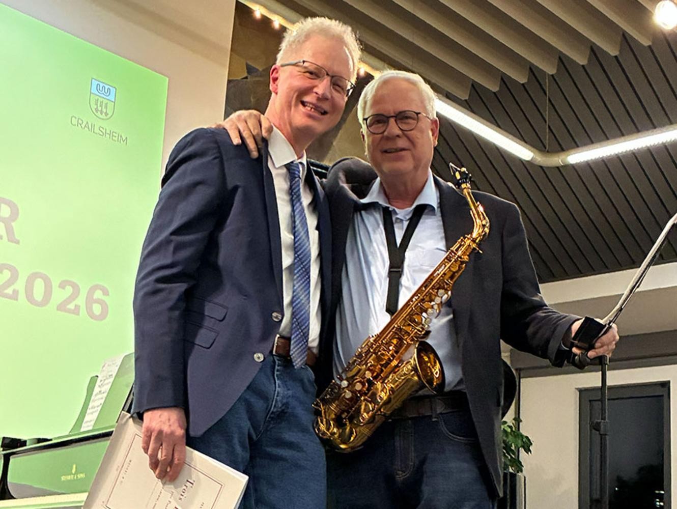 Zwei Männer, einer mit Saxophon, lächeln in die Kamera