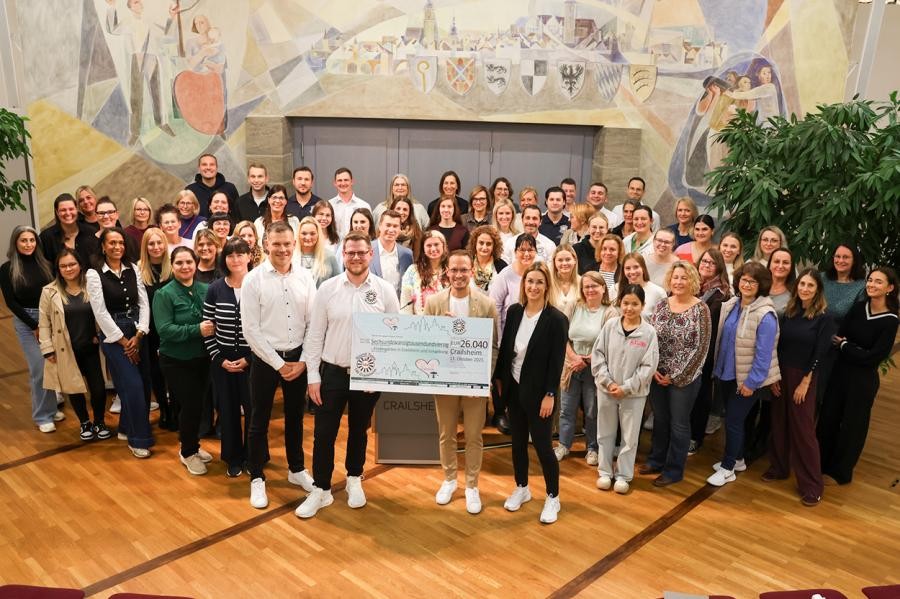 Eine große Gruppen Menschen steht in einem Saal zusammen und blickt in die Kamera, vier Personen vorne mit einem Symbolscheck