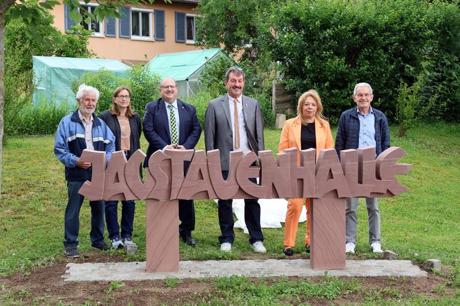 einige Personen stehen hinter einem steinernen Schriftzug "Jagstauenhalle"