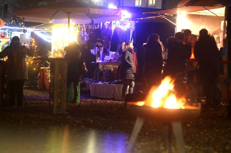 Menschen stehen an den Ständen und im Vordergrund brennt eine Feuerschaale