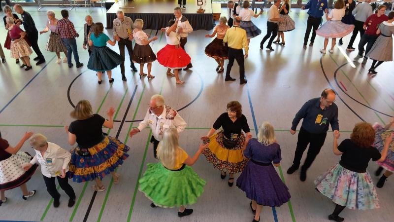 Tanzende Menschen in bunten Klamotten in einer Sport- und Festhalle