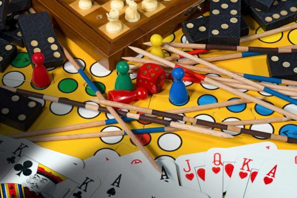 Verschiedene Spiele auf einem Haufen, darunter Mikado-Stäbe, Dominosteine, Karten und ein Mensch-Ärgere-Dich-Nicht-Spielbrett mit Würfel und Figuren