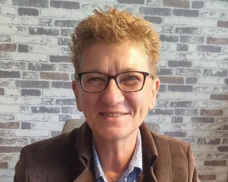 Eine Frau mit kurzen blonden Haaren, einer Brille und einem braunen Balzer