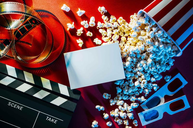 AdobeStock_116746669 Umgekippter Popcorneimer, Filmrolle, 3D-Brillen und eine Filmklappe