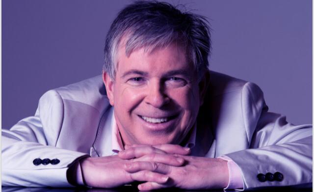 Portraitbild von einem Mann der seine Hände auf einem Tisch hat und darauf sein Kinn abgelegt