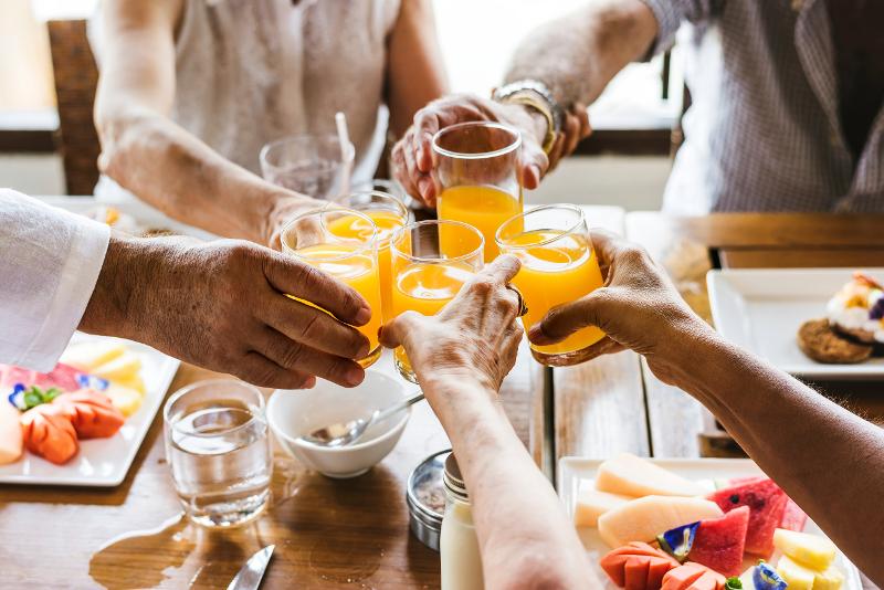 Bild auf dem verschiedene Hände mit einem Orangensaft über einem Frühstückstisch anstoßen