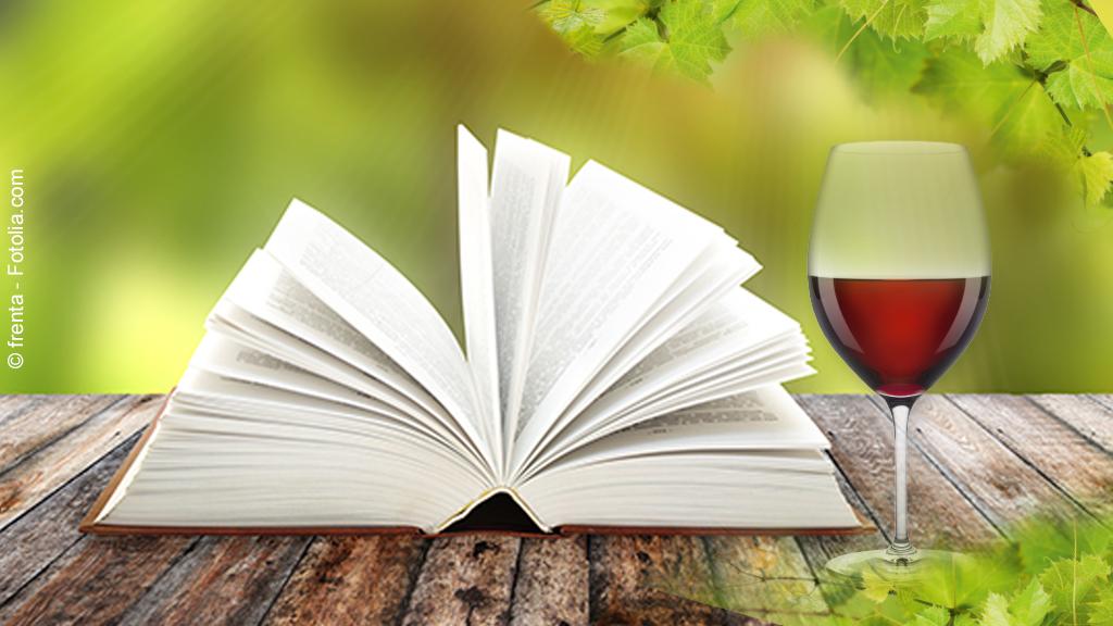 Ein geöffnetes Buch und ein volles Glas stehen und liegen auf einem Tisch