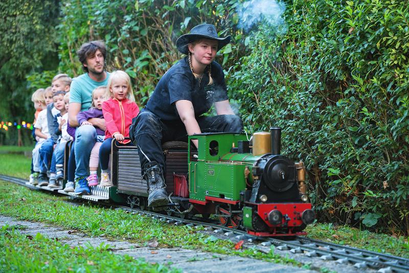 Dampfbahn mit Kindern, einem erwachsenen Mann und einer Schaffnerin fahren vorbei