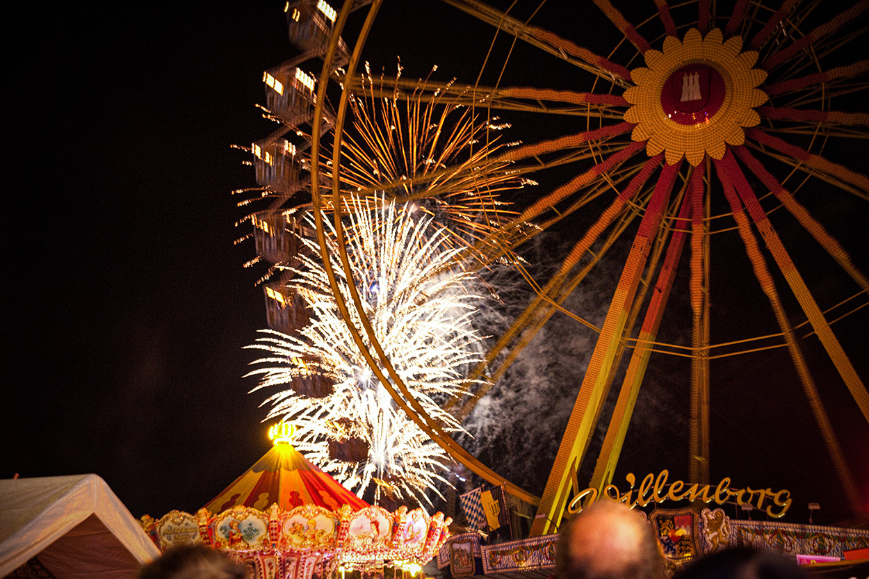 Ein Riesenrad bei Nacht, im Hintergrund ein leuchtendes Feuerwerk