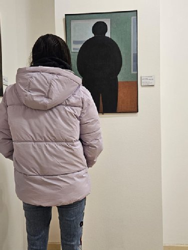Eine Frau im Anorak steht vor einem Bild, auf dem eine dunkle Gestalt zu sehen ist