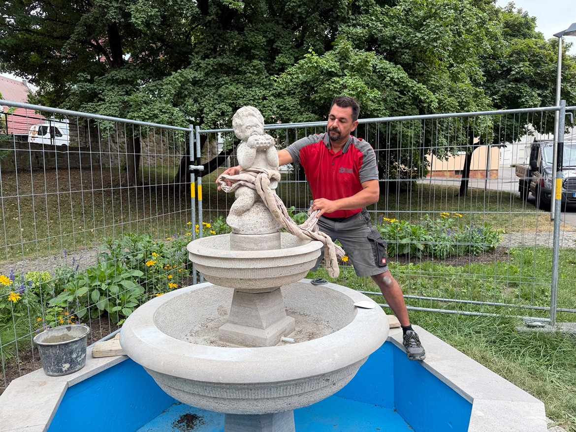 Ein Mann an einem Brunnen setzt die Figur oben auf