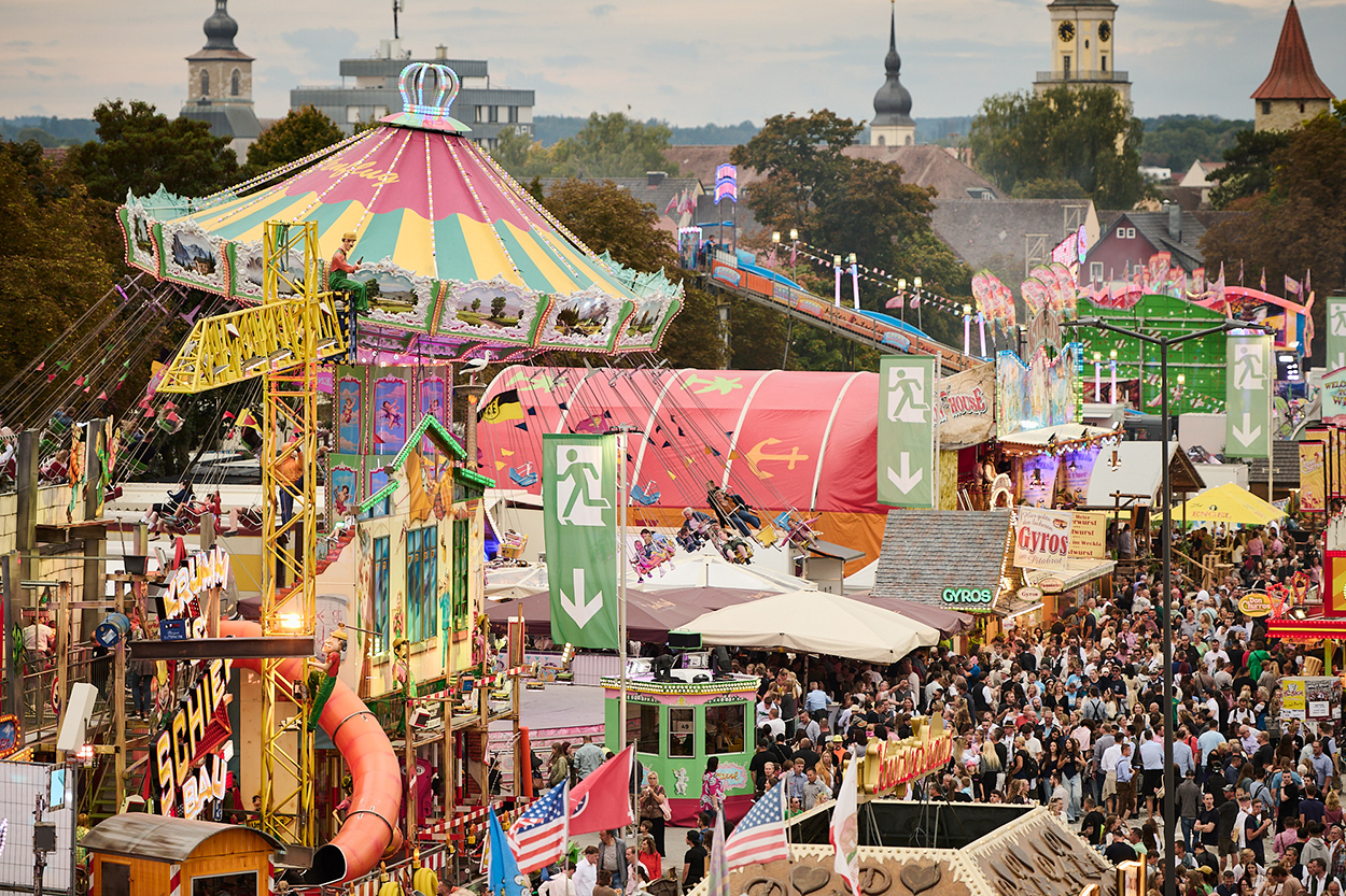 ein bunter Volksfestplatz mit vielen Fahrgeschäften und Menschen