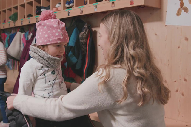 Erzieherin zieht Mädchen eine Jacke an. 