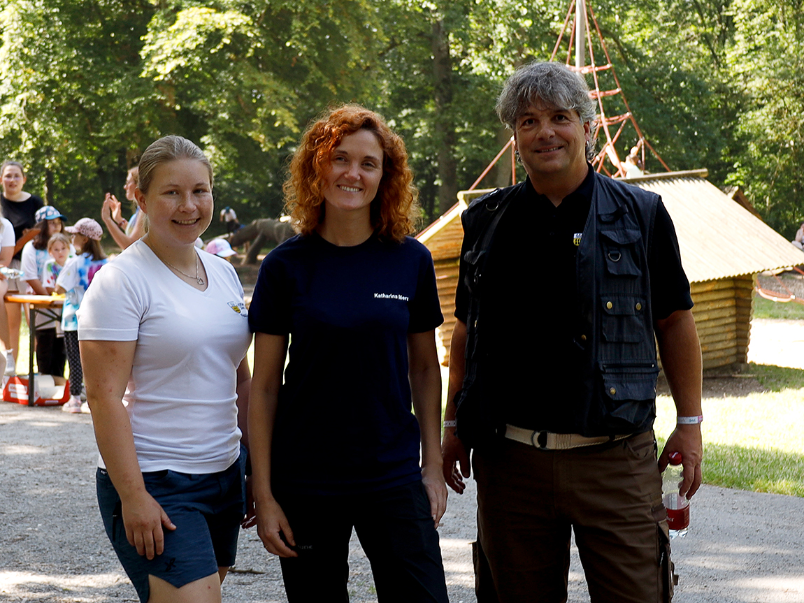 zwei Frauen und ein Mann lächeln an einem sommerlichen Tag in die Kamera