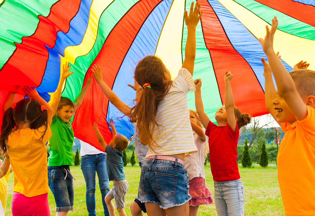Viele Kinder toben unter einem bunten aufgeblähten Fallschirm