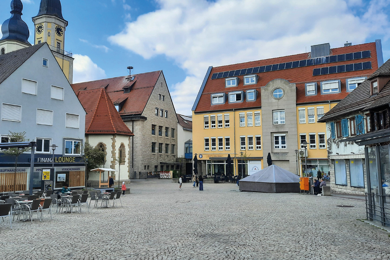 ein Platz in der Stadt mit Bestuhlung, Kapelle und einem noch abgedeckten Brunnen