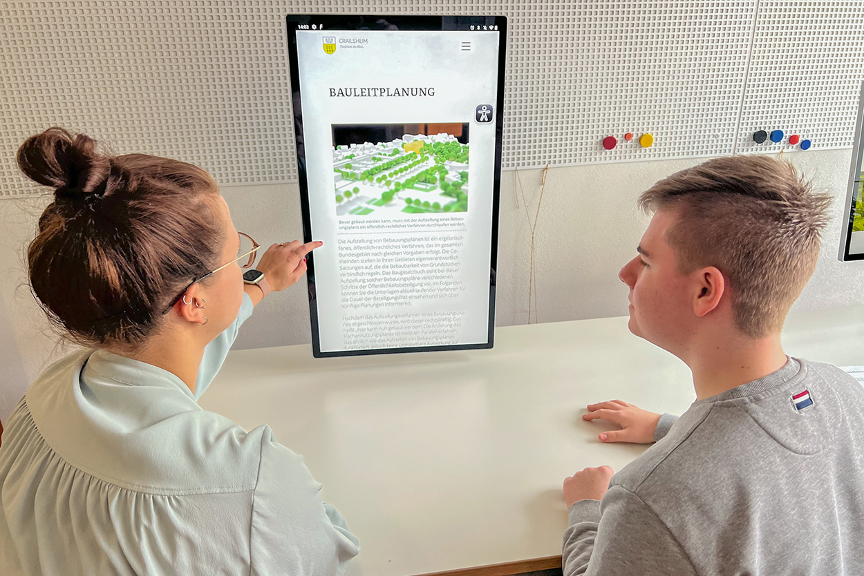 Stadtverwaltung Eine Frau und ein Mann sitzen an einem Tisch vor einem Display