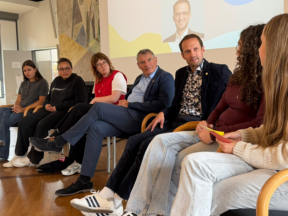 einige JUgendliche und zwei Herren sitzen auf Stühlen und sind in ein Gespräch vertieft