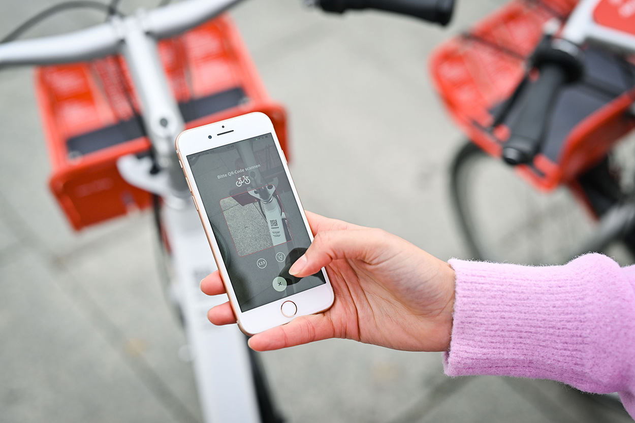 eine Hand hält ein Smartphone, im Hintergrund stehen Fahrräder