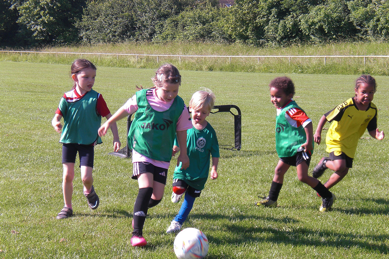 Kindergarten Kleeblatt Einige kleine Kinder in Fußballtrikots rennen einem Ball nach.
