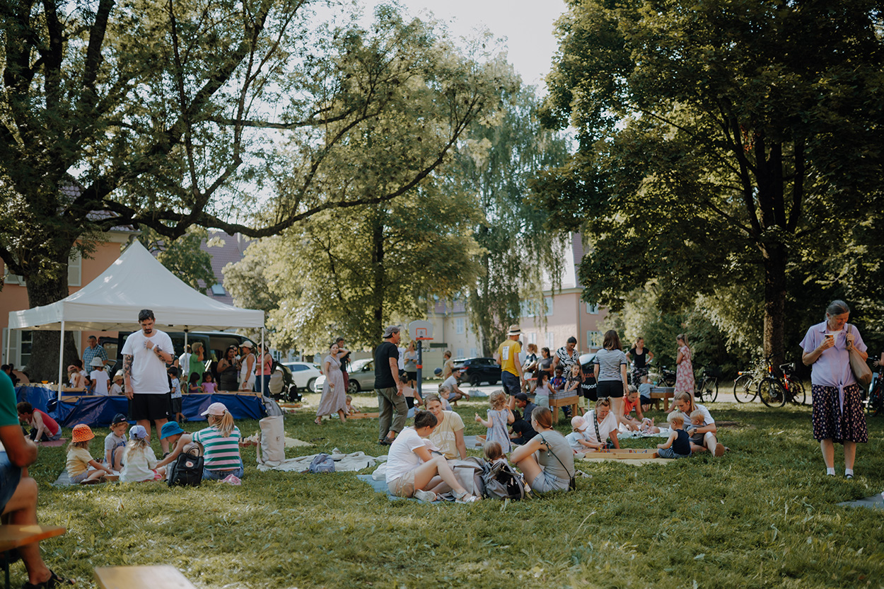 Viele Menschen auf einer Wiese unter Bäumen und Zelten