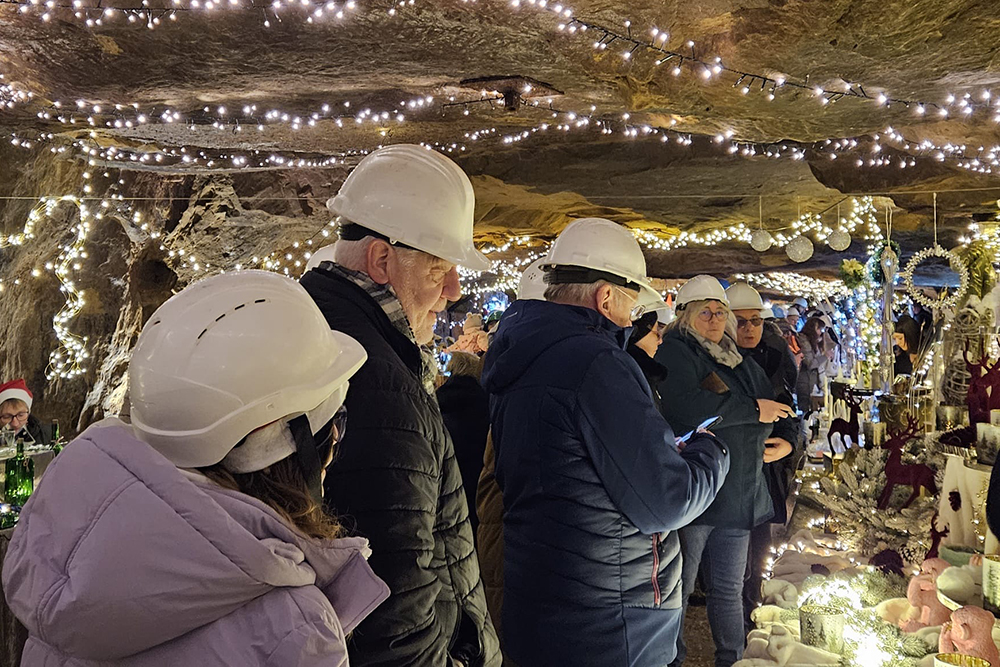Mehrere Menschen mit Sicherheitshelmen besuchen Stände in einem Bergwerksstollen