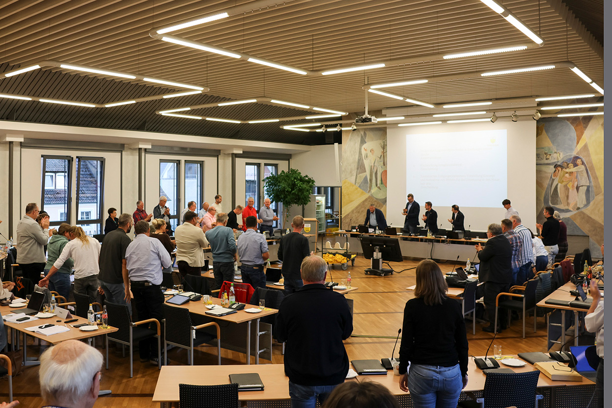 Viele Menschen stehen an Tischen in einem Saal und klatschen