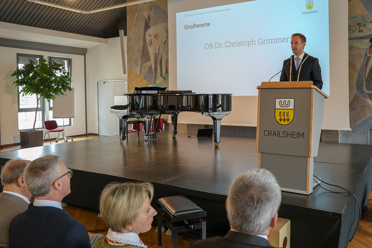 Ein Mann mit Amtskette steht an einem Rednerpult auf einer Bühne, davor lauschendes Publikum