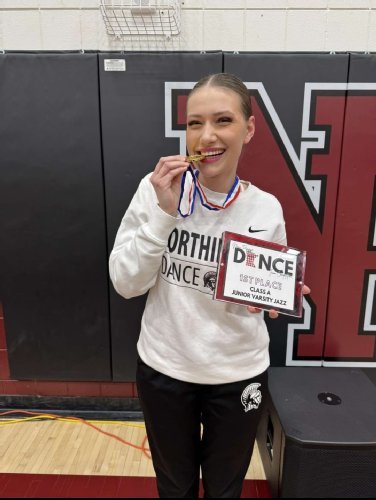 Eine junge Frau im Trainingsazug beißt lächelnd auf eine Medaille und hat eine Urkunde in der Hand.