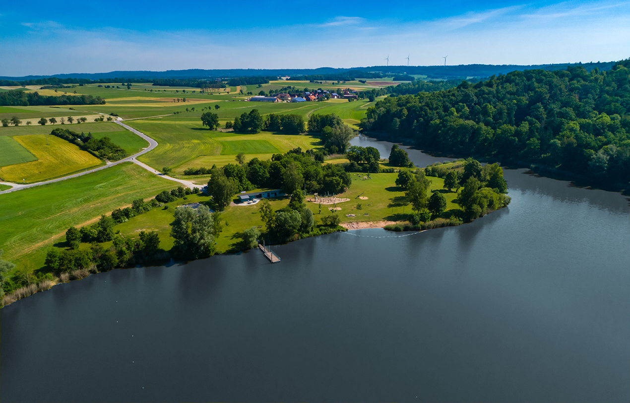 Ein idyllischer See aus der Vogelperspektive mit viel Grün.