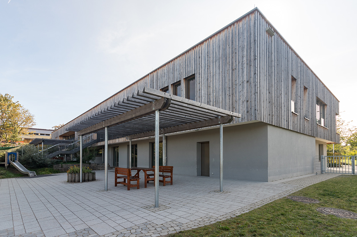 Ein gepflastereter Hof vor einem Haus mit Holz verkeldiet und einer Überdachung