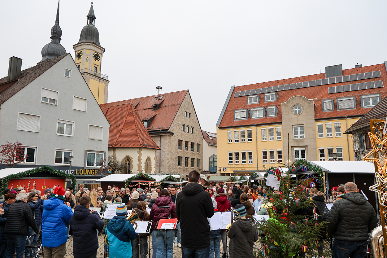 Viele Menschen auf einem Platz, auf dem eine Kapelle spielt und Weihnachtsbuden stehen