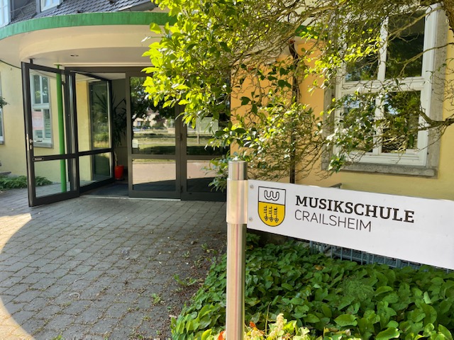 der Eingang zu einem Gebäude, davor ein Schild auf dem Musikschule steht