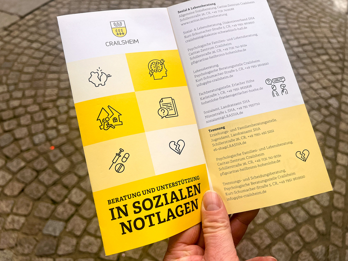 Ein gelb-weißer Flyer mit der Schrift "In sozialen Notlagen", dahinter sind Pflastersteine zu sehen