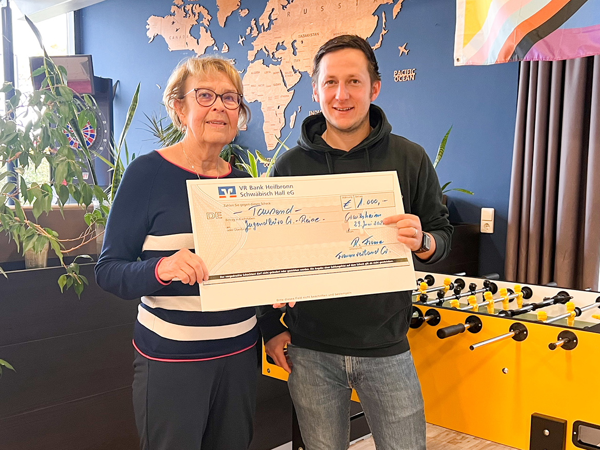 Eine Frau und ein Mann halten einen übergroßen Scheck und sehen in die Kamera