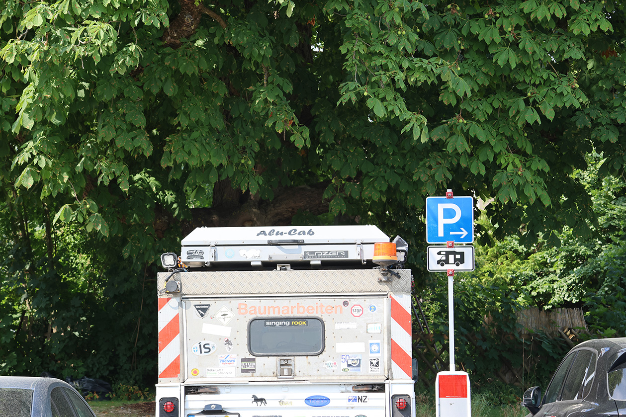 Das Heck eines großen Fahrzeugs, daneben ein Schild, das auf Wohnmobilstellplätze hinweist