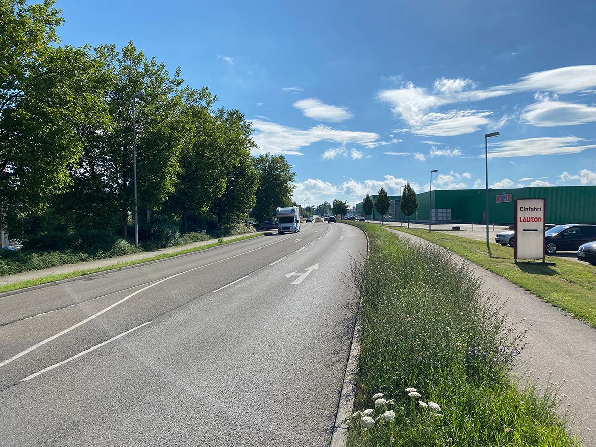 Stadtverwaltung Eine Straße mit eingen Fahrbahnschäden bei Sonnenschein.