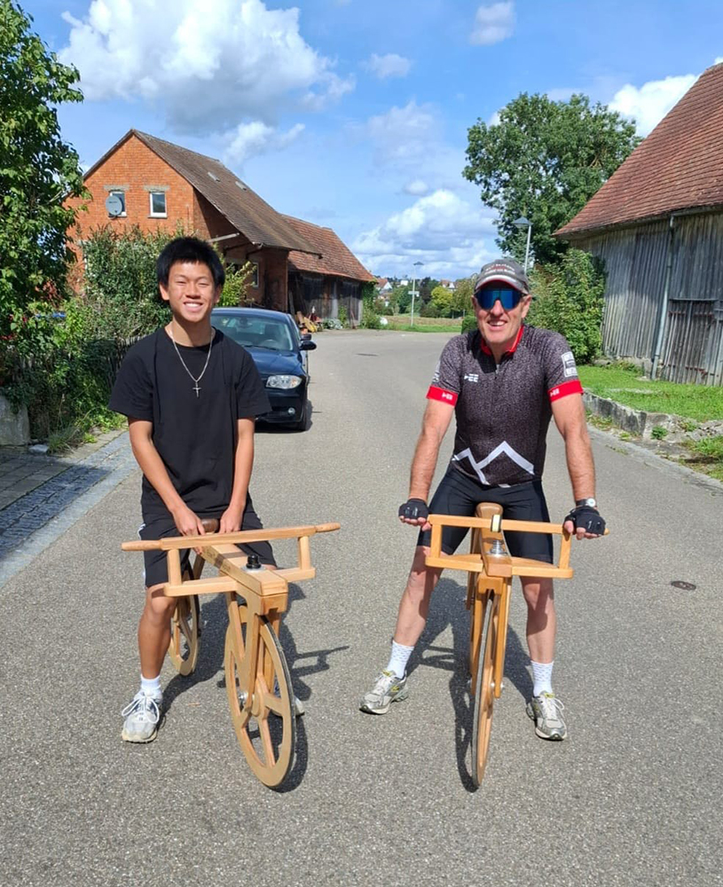 zwei Männer mit hölzernen Draisrädern lächenln in die Kamera