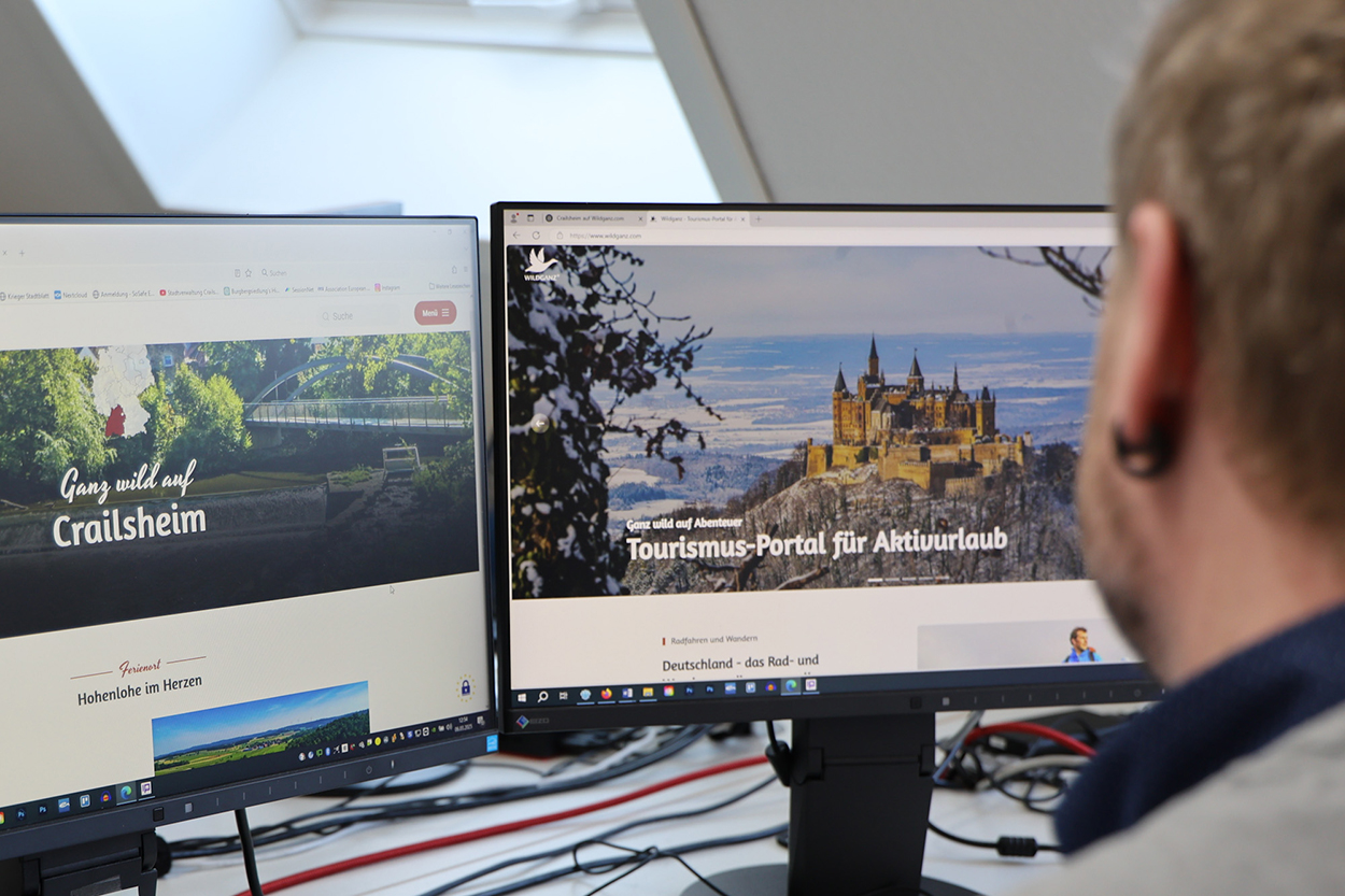 Stadtverwaltung Ein Mann sieht vor zwei Bildschirmen und sieht sich die Seite wildganz.com an