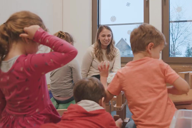 Erzieherin und Kinder sitzen zusammen auf dem Boden.