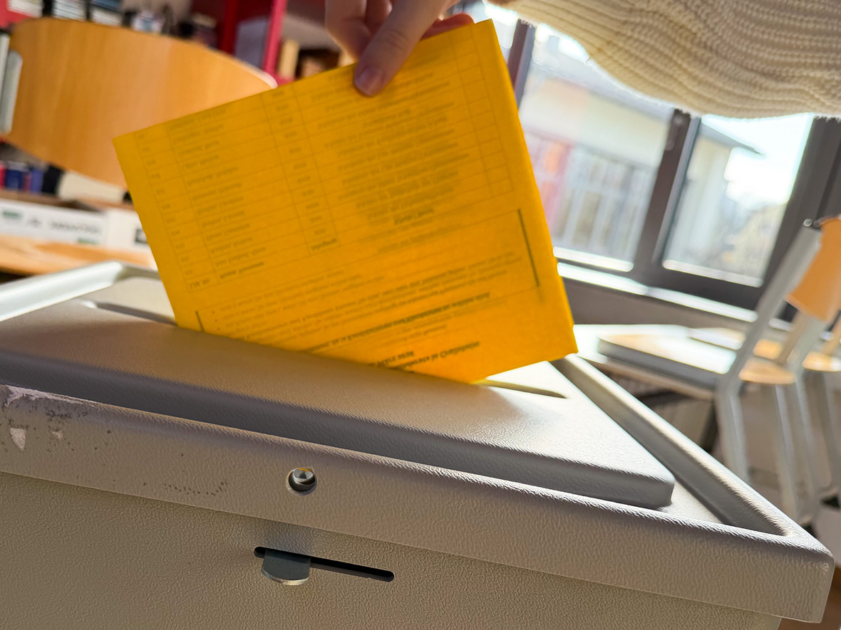 Ein gelber Wahlzettel wird in eine Urne gesteckt.