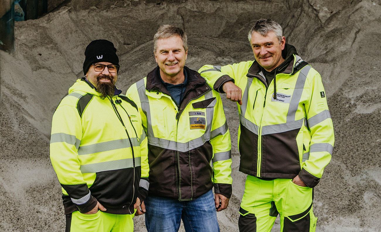 Drei Männer in neongelber Arbeitskleidung lächeln in die Kamera