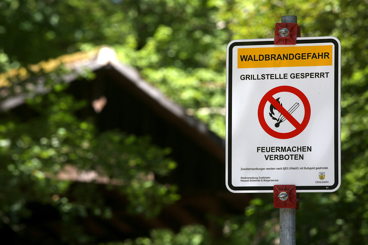 Ein Schild, das auf Waldbrandgefahr und eine gesperrte Grillstelle aufmerksam macht, dahinter eine Hütte im Wald