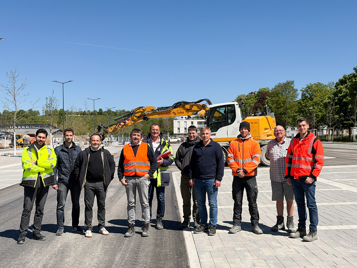 Einige Männer teils in Arbeitskleidung stehen vor einem Bagger für ein Foto parat