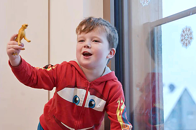 Junge hält einen Spielzeug-Dinosaurier fest.