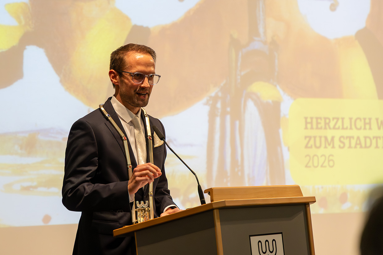 Ein Mann mit Amtskette steht an einem Rednerpult vor einer Leinwand