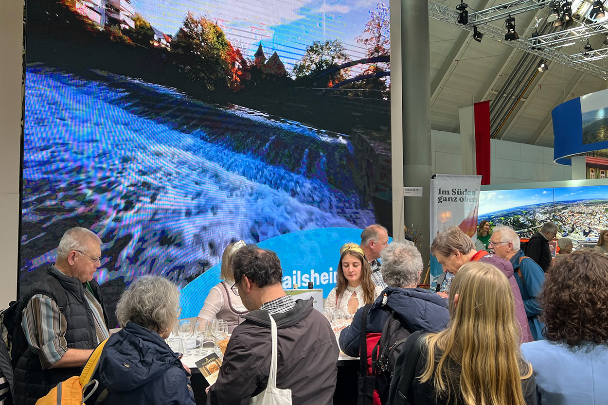 viele Menschen an einem Messesatnd, im Hintergrund ein Bild von einem Fluss